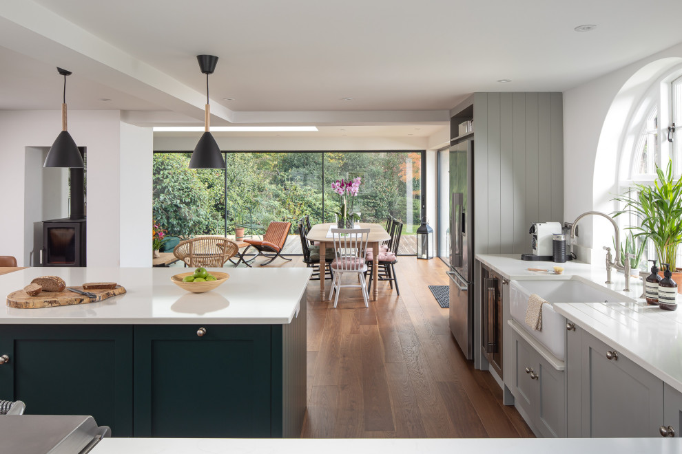 Design ideas for a large rural l-shaped open plan kitchen in Berkshire with a belfast sink, flat-panel cabinets, grey cabinets, an island and white worktops.