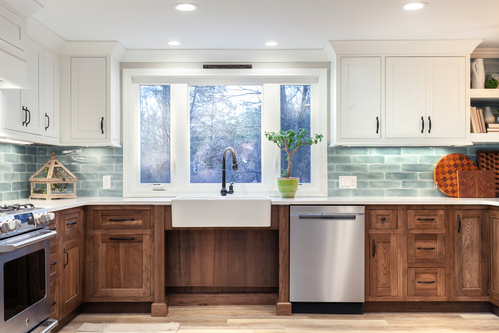 This is an example of a large transitional u-shaped eat-in kitchen in Bridgeport with a farmhouse sink, recessed-panel cabinets, brown cabinets, quartz benchtops, blue splashback, subway tile splashback, stainless steel appliances, light hardwood floors, no island, beige floor and white benchtop.