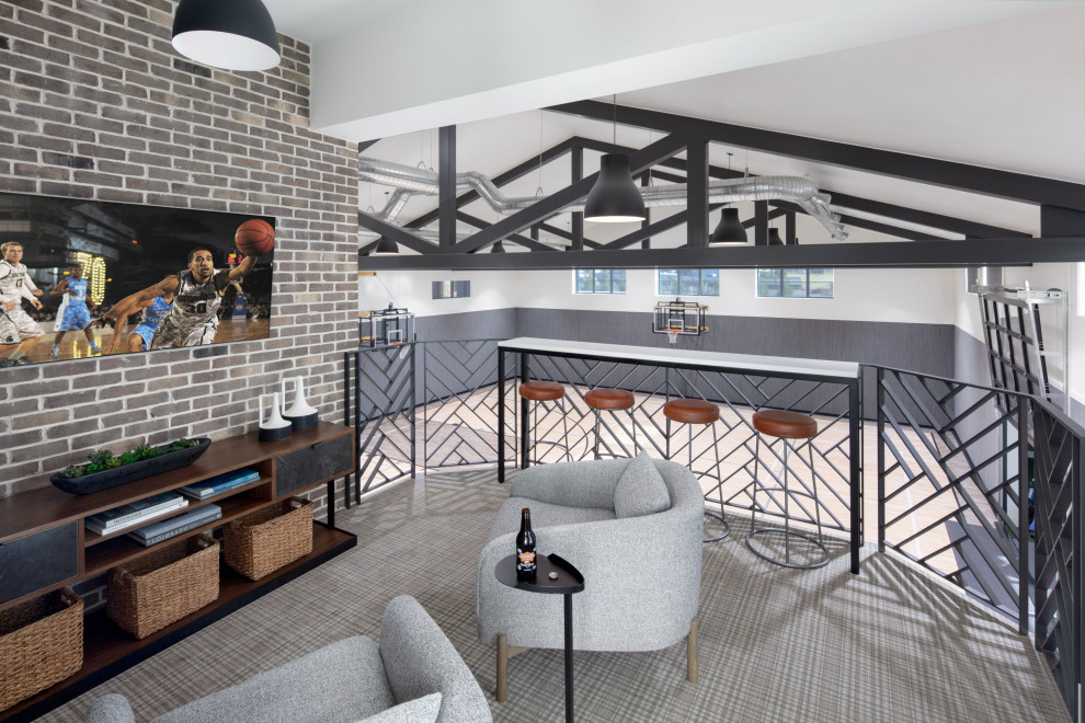 Luxury Custom Home Gym Basketball Court Overlook - This luxury custom home has it all, including a full-sized indoor basketball court. This overlook is set just off the kitchen and family room, so spectators can watch basketball games or pickleball match going on below. The geometric metal railings, patterned carpet, and exposed brick wall add charm to the gym overlook. Barstools overlook the gym.