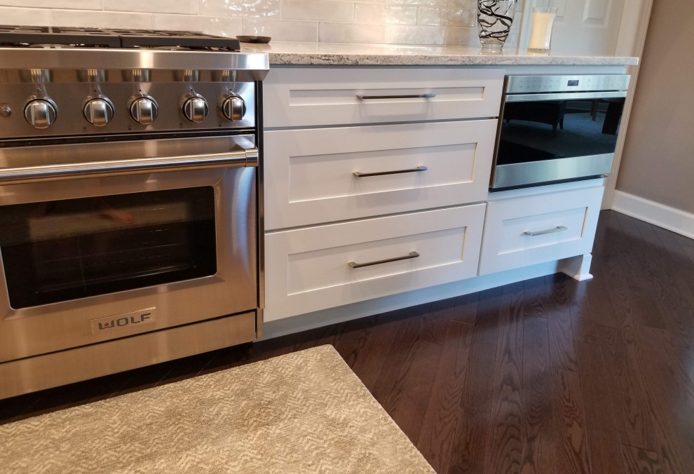 Example of a transitional l-shaped dark wood floor and brown floor kitchen design in Chicago with shaker cabinets, white cabinets, quartz countertops and an island