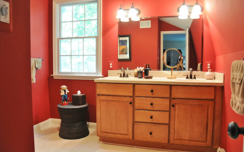 This is an example of a mid-sized country 3/4 bathroom in Baltimore with raised-panel cabinets, light wood cabinets, an alcove shower, beige tile, ceramic tile, red walls, ceramic floors, an undermount sink and laminate benchtops.