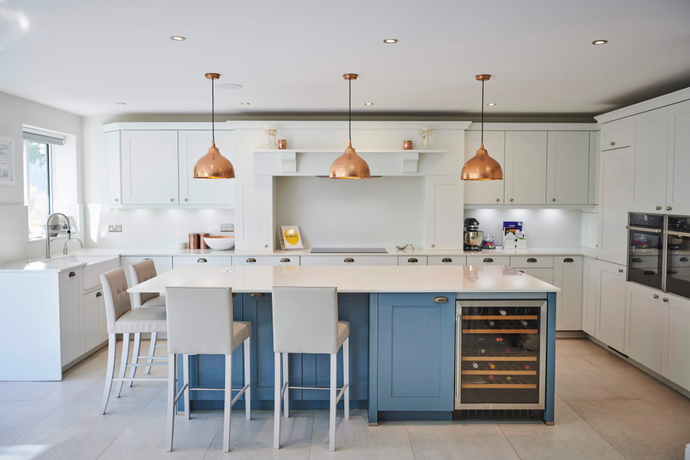 Large transitional galley kitchen in Hertfordshire with an integrated sink, shaker cabinets, blue cabinets, quartzite benchtops, white splashback, black appliances, porcelain floors, a peninsula, grey floor and white benchtop.