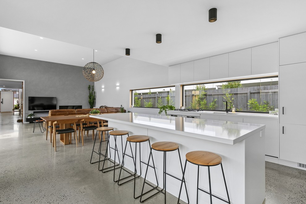 This is an example of a large contemporary galley open plan kitchen in Geelong with a double-bowl sink, flat-panel cabinets, white cabinets, quartz benchtops, window splashback, stainless steel appliances, concrete floors, with island, white benchtop and grey floor.