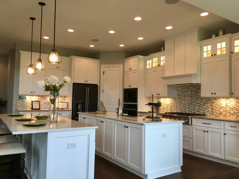 Photo of a large transitional l-shaped eat-in kitchen in Milwaukee with a farmhouse sink, recessed-panel cabinets, white cabinets, quartz benchtops, multi-coloured splashback, ceramic splashback, stainless steel appliances, medium hardwood floors, multiple islands, brown floor and multi-coloured benchtop.