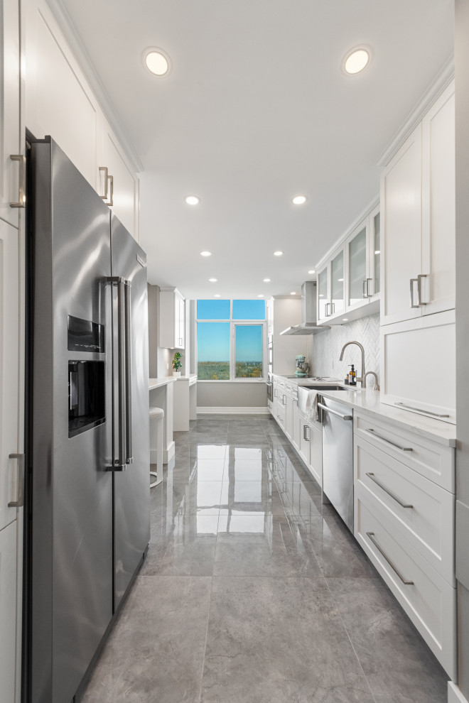 This is an example of a mid-sized contemporary galley kitchen pantry in Ottawa with a farmhouse sink, shaker cabinets, white cabinets, quartzite benchtops, white splashback, ceramic splashback, stainless steel appliances, porcelain floors, a peninsula, grey floor and white benchtop.