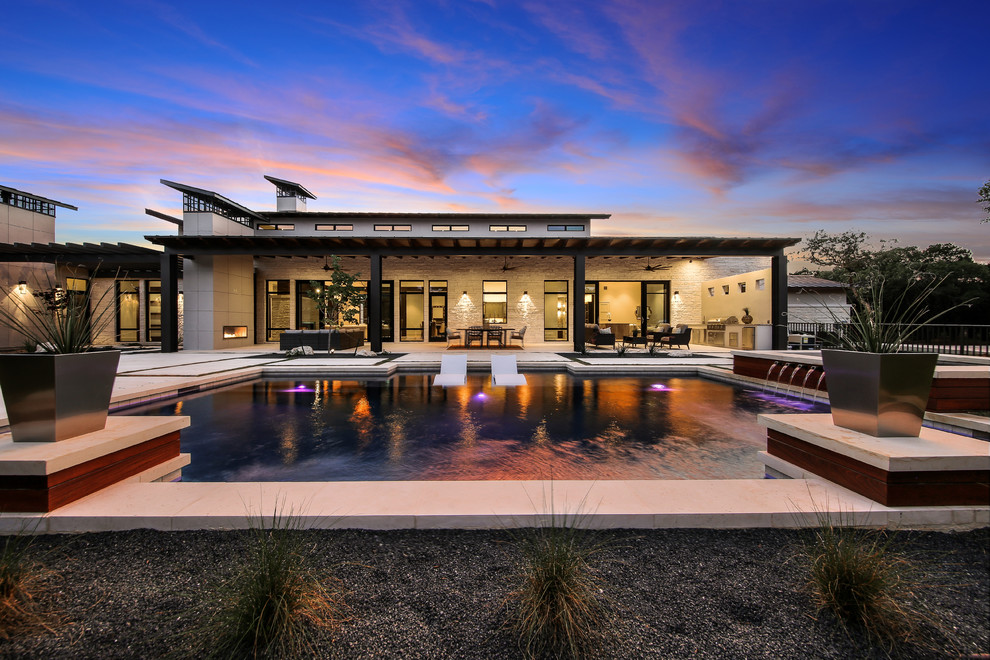 This is an example of a large transitional backyard rectangular natural pool in Austin with a pool house and natural stone pavers.