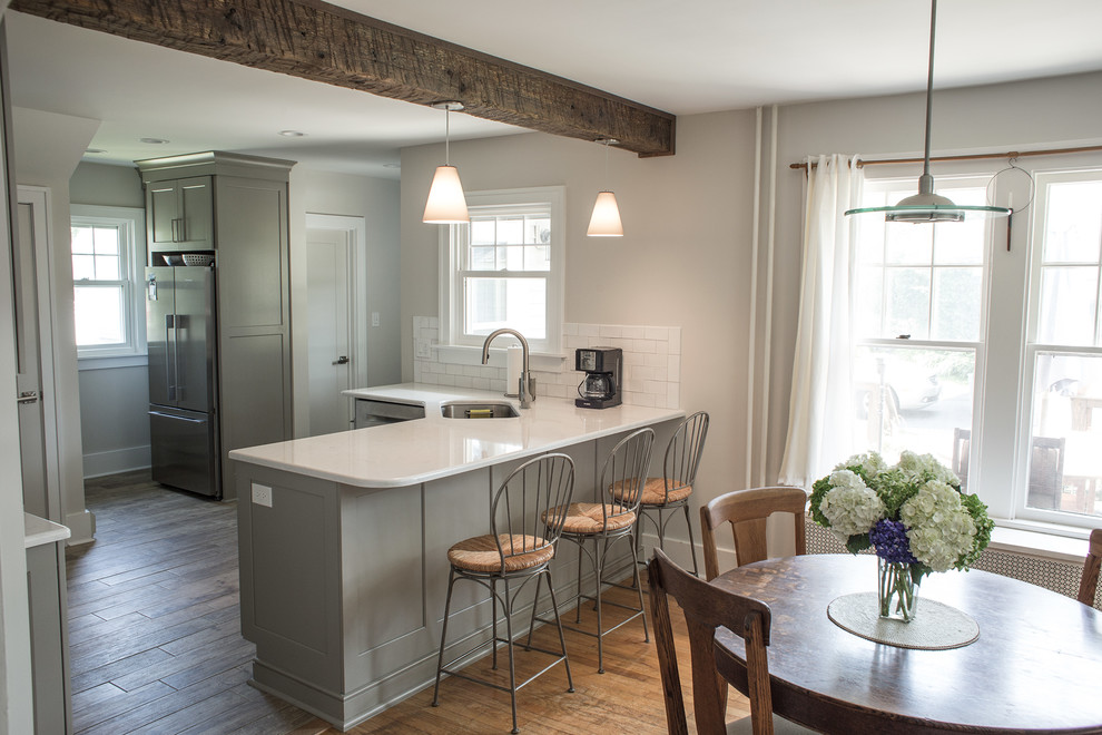 Photo of a mid-sized transitional u-shaped eat-in kitchen in Boston with an undermount sink, grey cabinets, white splashback, medium hardwood floors, a peninsula, recessed-panel cabinets and stainless steel appliances.