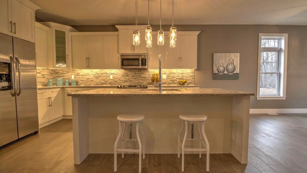 Example of a mid-sized transitional l-shaped medium tone wood floor and brown floor open concept kitchen design with shaker cabinets, white cabinets, granite countertops, an island, an undermount sink, gray backsplash, matchstick tile backsplash, stainless steel appliances and gray countertops