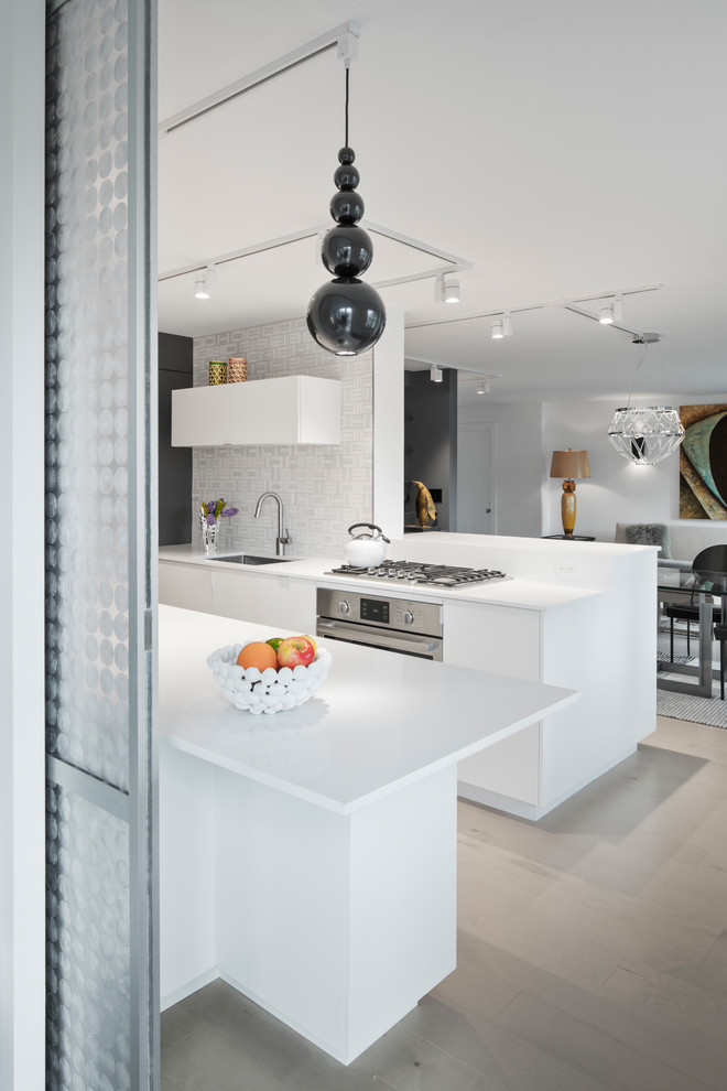 This is an example of a mid-sized contemporary galley eat-in kitchen in New York with white cabinets, stainless steel appliances, beige floor, white benchtop, an undermount sink, flat-panel cabinets, quartz benchtops, white splashback, ceramic splashback and light hardwood floors.