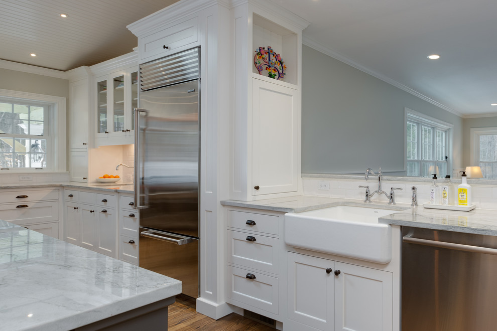 Inspiration for a large beach style l-shaped eat-in kitchen in Boston with a farmhouse sink, recessed-panel cabinets, white cabinets, quartzite benchtops, white splashback, subway tile splashback, stainless steel appliances, medium hardwood floors and with island.