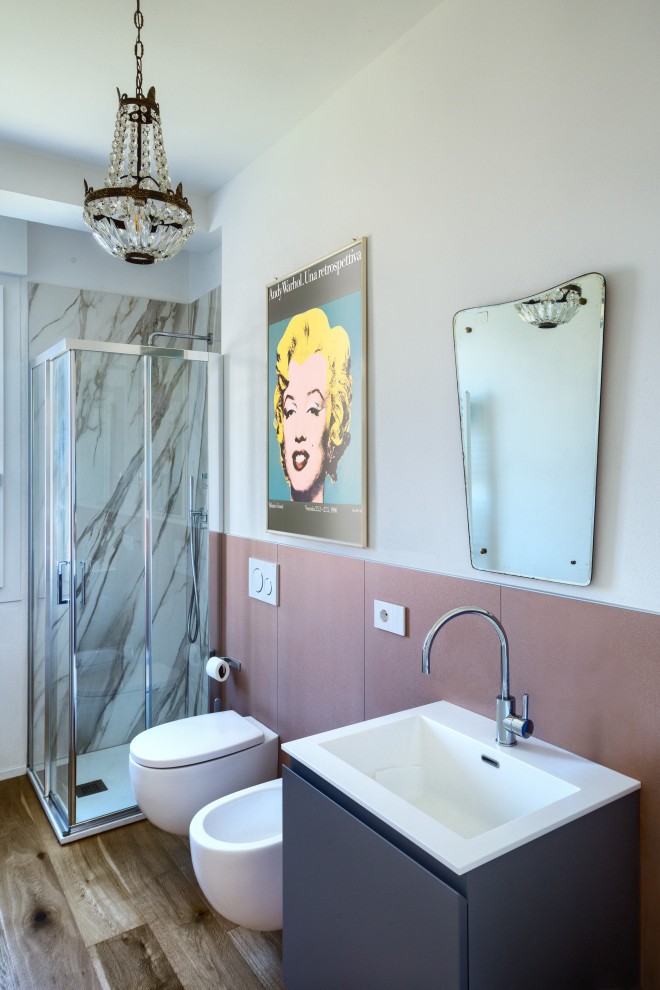 Inredning av ett modernt litet toalett, med grå skåp, en vägghängd toalettstol, rosa kakel, porslinskakel, vita väggar, ljust trägolv och ett väggmonterat handfat