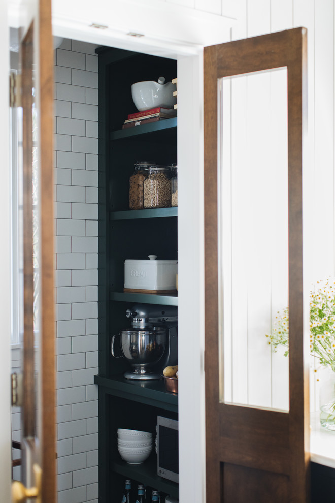 Inspiration for a mid-sized transitional l-shaped medium tone wood floor and brown floor kitchen pantry remodel in Chicago with a farmhouse sink, shaker cabinets, black cabinets, marble countertops, white backsplash, marble backsplash, paneled appliances and an island
