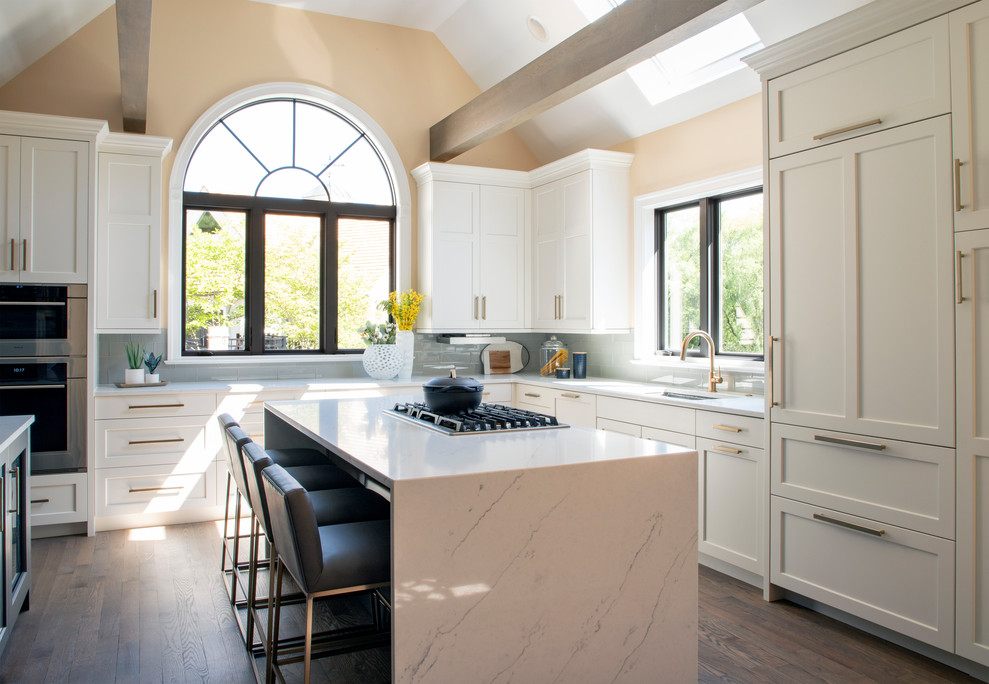 Inspiration for a large transitional u-shaped medium tone wood floor kitchen remodel with an undermount sink, white cabinets, quartz countertops, gray backsplash, glass tile backsplash, stainless steel appliances, an island and white countertops