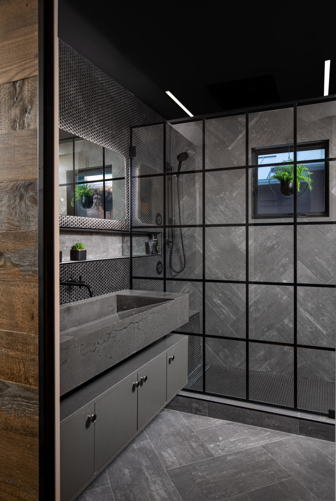 Bild på ett mellanstort industriellt grå grått en-suite badrum, med släta luckor, grå skåp, våtrum, en vägghängd toalettstol, svart kakel, keramikplattor, grå väggar, klinkergolv i keramik, ett avlångt handfat, bänkskiva i betong, grått golv och dusch med gångjärnsdörr