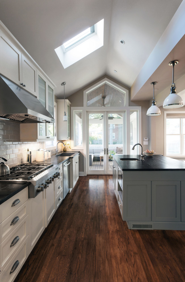 Example of a mid-sized minimalist single-wall dark wood floor open concept kitchen design in DC Metro with a farmhouse sink, recessed-panel cabinets, gray cabinets, soapstone countertops, gray backsplash, subway tile backsplash, stainless steel appliances and an island