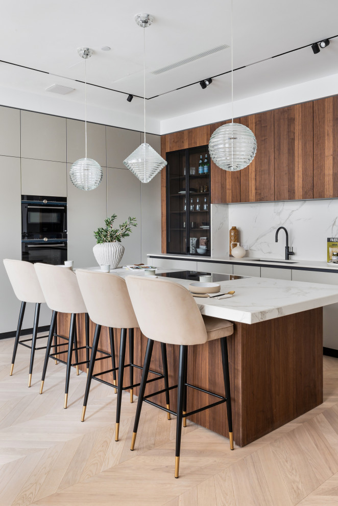 Photo of a contemporary l-shaped kitchen in London with an undermount sink, flat-panel cabinets, grey cabinets, white splashback, black appliances, light hardwood floors, with island, beige floor and white benchtop.