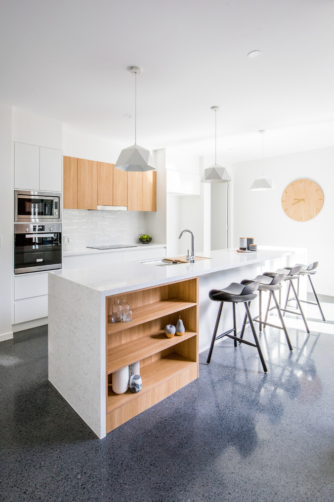 Photo of a beach style galley eat-in kitchen in Gold Coast - Tweed with an undermount sink, flat-panel cabinets, white cabinets, white splashback, stainless steel appliances and with island.