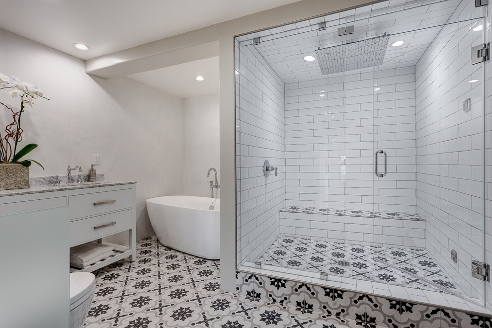 Inspiration for a large mediterranean master bathroom in Los Angeles with flat-panel cabinets, a freestanding tub, an alcove shower, a one-piece toilet, white tile, subway tile, white walls, an integrated sink, marble benchtops, white cabinets, multi-coloured floor, a hinged shower door and cement tiles.