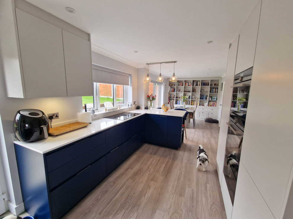 Small contemporary l-shaped eat-in kitchen in Other with an undermount sink, flat-panel cabinets, blue cabinets, quartzite benchtops, beige splashback, engineered quartz splashback, black appliances, light hardwood floors, no island, brown floor and beige benchtop.