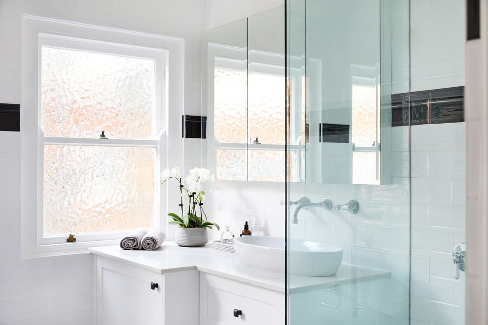 This is an example of a traditional bathroom in Sydney with recessed-panel cabinets, white cabinets, a corner shower, black tile, white tile, white walls, a vessel sink and white benchtops.
