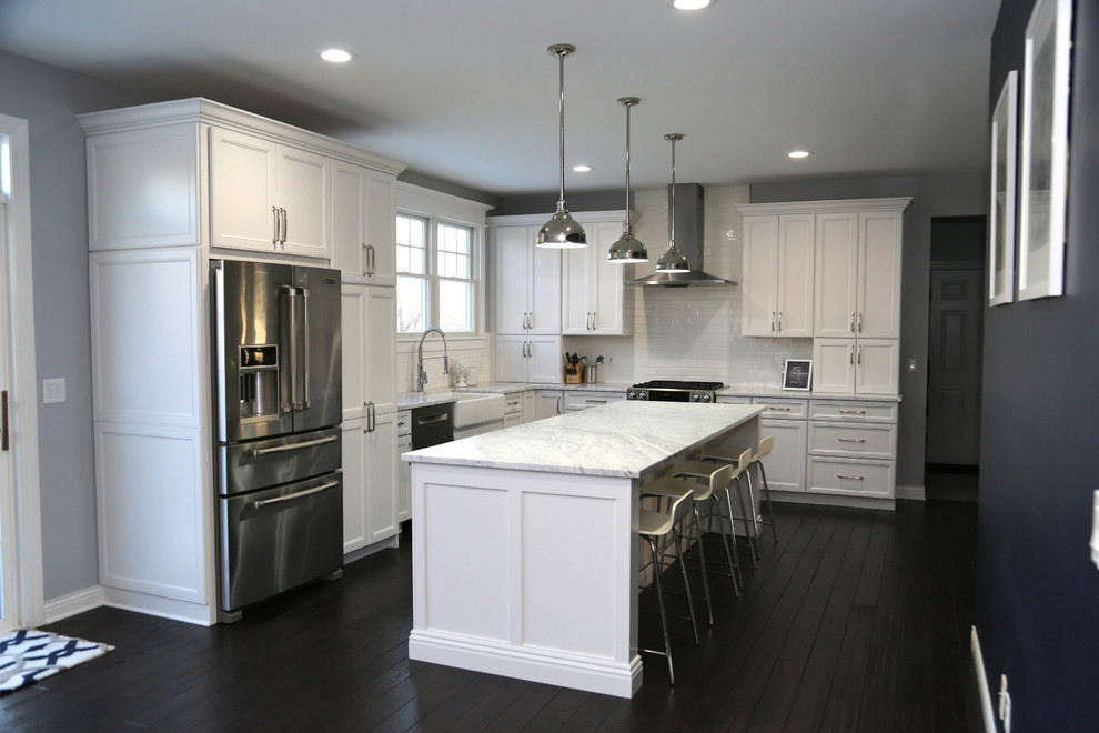 Inspiration for a large transitional l-shaped dark wood floor eat-in kitchen remodel in Chicago with recessed-panel cabinets, stainless steel appliances, an island, a farmhouse sink, white cabinets, quartz countertops, white backsplash and subway tile backsplash
