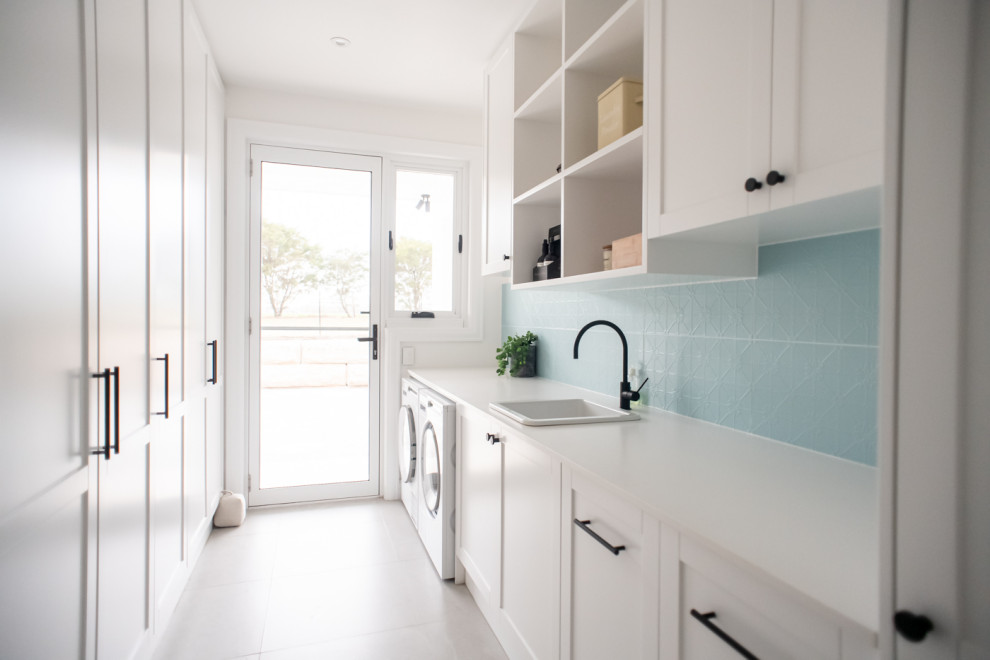 Large modern galley separated utility room in Sydney with a built-in sink, shaker cabinets, white cabinets, engineered stone countertops, blue splashback, ceramic splashback, blue walls, ceramic flooring, a side by side washer and dryer, grey floors and white worktops.