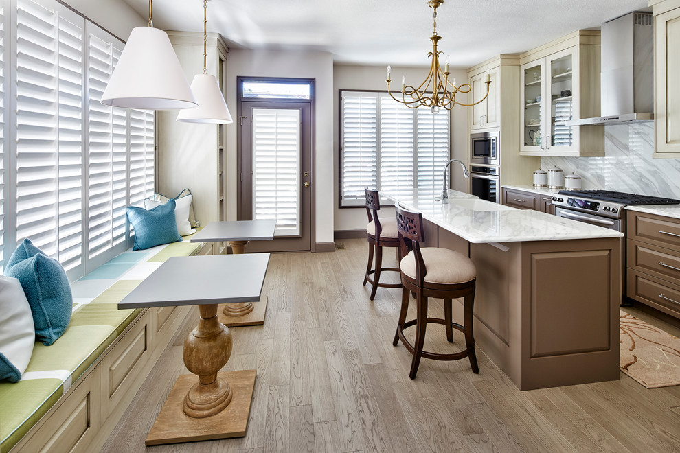 Photo of a mid-sized transitional l-shaped eat-in kitchen in Denver with a farmhouse sink, brown cabinets, multi-coloured splashback, stainless steel appliances, medium hardwood floors, with island, brown floor and multi-coloured benchtop.