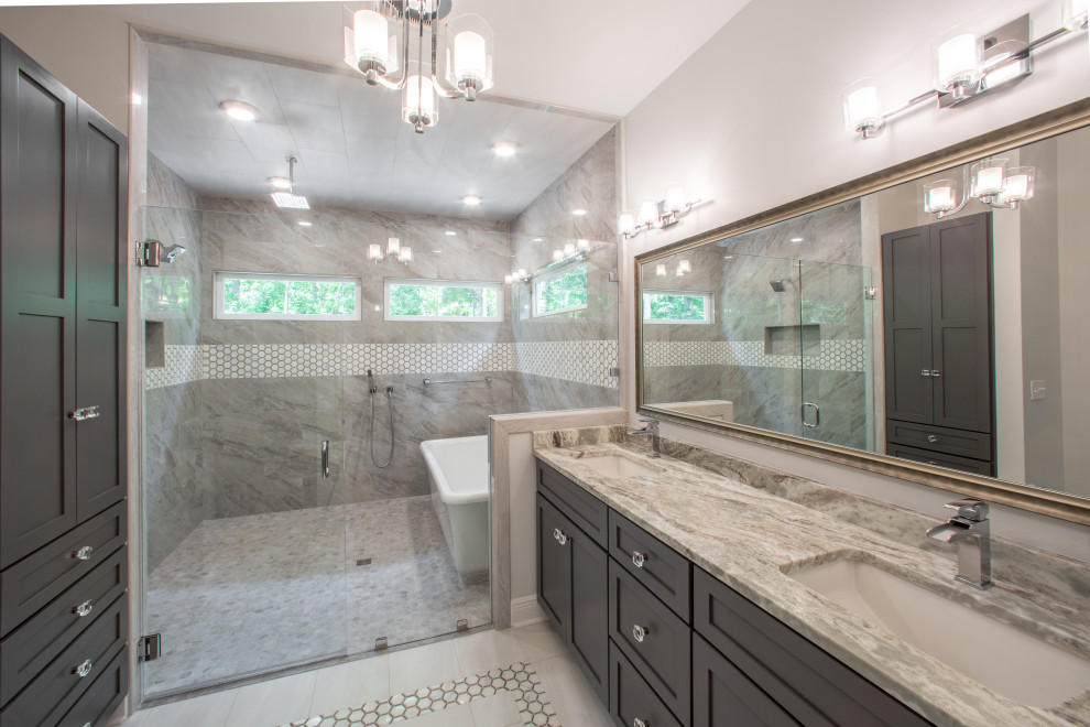 This is an example of a mid-sized traditional master bathroom with recessed-panel cabinets, grey cabinets, a freestanding tub, a curbless shower, a one-piece toilet, multi-coloured tile, porcelain tile, white walls, porcelain floors, an integrated sink, quartzite benchtops, white floor, a hinged shower door, multi-coloured benchtops, an enclosed toilet, a double vanity and a built-in vanity.