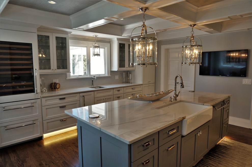 This is an example of a large traditional galley open plan kitchen in Other with a farmhouse sink, shaker cabinets, white cabinets, marble benchtops, white splashback, glass tile splashback, stainless steel appliances, dark hardwood floors, with island and brown floor.