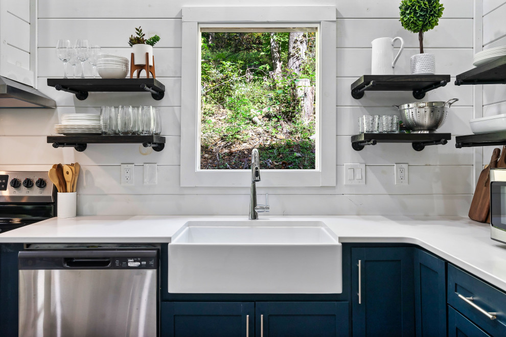 This is an example of a mid-sized modern l-shaped open plan kitchen in Houston with a farmhouse sink, recessed-panel cabinets, blue cabinets, white splashback, shiplap splashback, stainless steel appliances, dark hardwood floors, no island, brown floor, white benchtop and vaulted.