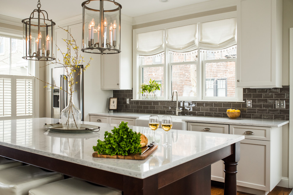 This is an example of a transitional kitchen in Boston with a farmhouse sink, recessed-panel cabinets, white cabinets, grey splashback, subway tile splashback, stainless steel appliances, dark hardwood floors, with island, brown floor and white benchtop.