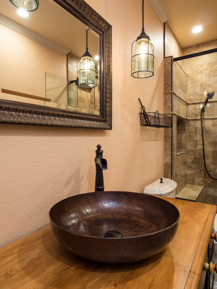 Mid-sized country bathroom in Orlando with furniture-like cabinets, distressed cabinets, a curbless shower, a two-piece toilet, beige tile, travertine, beige walls, travertine floors, a vessel sink, wood benchtops, beige floor and a hinged shower door.