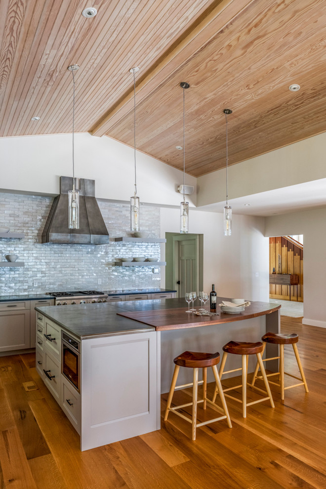 This is an example of an expansive modern l-shaped open plan kitchen in Portland Maine with recessed-panel cabinets, grey cabinets, zinc benchtops, grey splashback, subway tile splashback, stainless steel appliances, medium hardwood floors and with island.