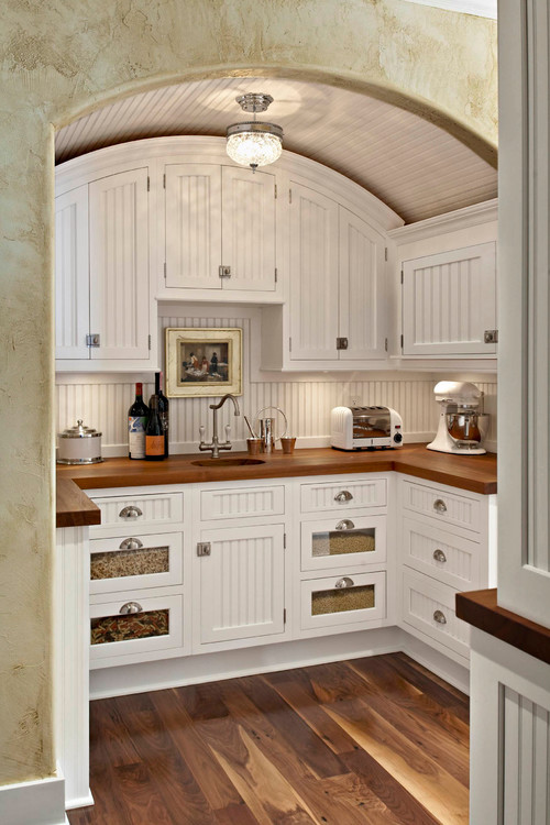 Arched ceiling pantry with white cabinets and dark wood countertop