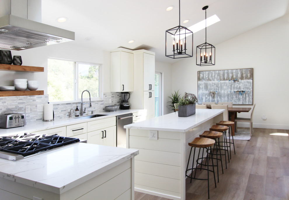 Example of a mid-sized transitional l-shaped vinyl floor, brown floor and vaulted ceiling eat-in kitchen design with an undermount sink, shaker cabinets, white cabinets, quartz countertops, multicolored backsplash, mosaic tile backsplash, stainless steel appliances, an island and white countertops