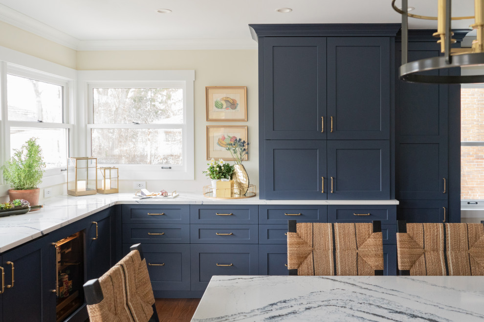 Klassisk inredning av ett mellanstort vit vitt kök, med en undermonterad diskho, skåp i shakerstil, blå skåp, bänkskiva i kvarts, vitt stänkskydd, stänkskydd i keramik, rostfria vitvaror, mellanmörkt trägolv, en köksö och brunt golv