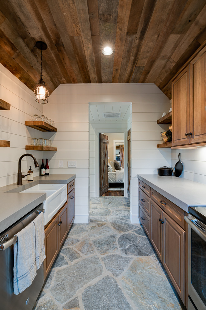 Example of a mid-sized mountain style galley slate floor enclosed kitchen design with a farmhouse sink, raised-panel cabinets, medium tone wood cabinets, quartz countertops, stainless steel appliances and no island