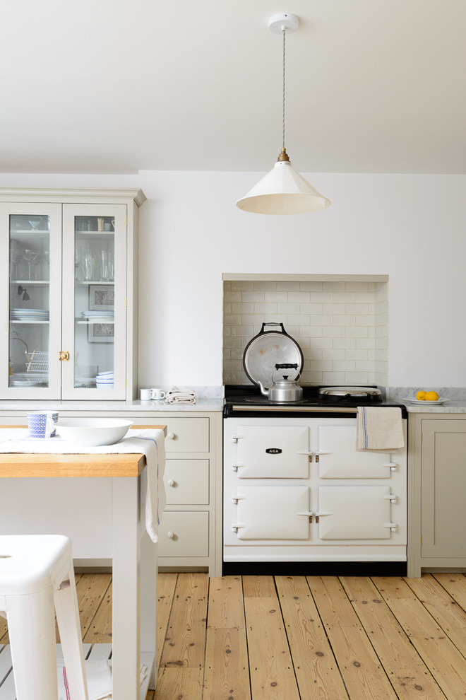 This is an example of a mid-sized country u-shaped open plan kitchen in Sussex with a farmhouse sink, shaker cabinets, grey cabinets, marble benchtops, white splashback, subway tile splashback, white appliances, light hardwood floors and with island.