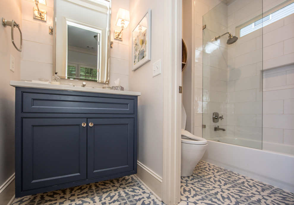 This is an example of a mid-sized eclectic 3/4 bathroom in Atlanta with beaded inset cabinets, blue cabinets, an alcove tub, an alcove shower, a one-piece toilet, white tile, ceramic tile, white walls, porcelain floors, an undermount sink, engineered quartz benchtops, blue floor, an open shower, white benchtops, an enclosed toilet, a single vanity and a freestanding vanity.