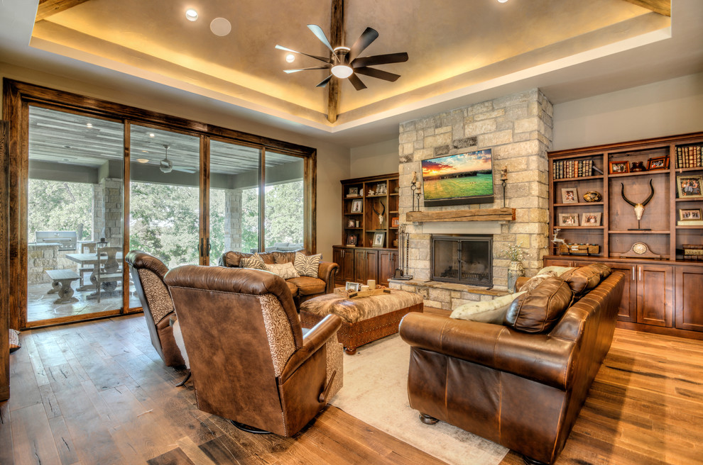 Transitional open concept family room in Austin with beige walls, medium hardwood floors, a standard fireplace, a stone fireplace surround and a wall-mounted tv.