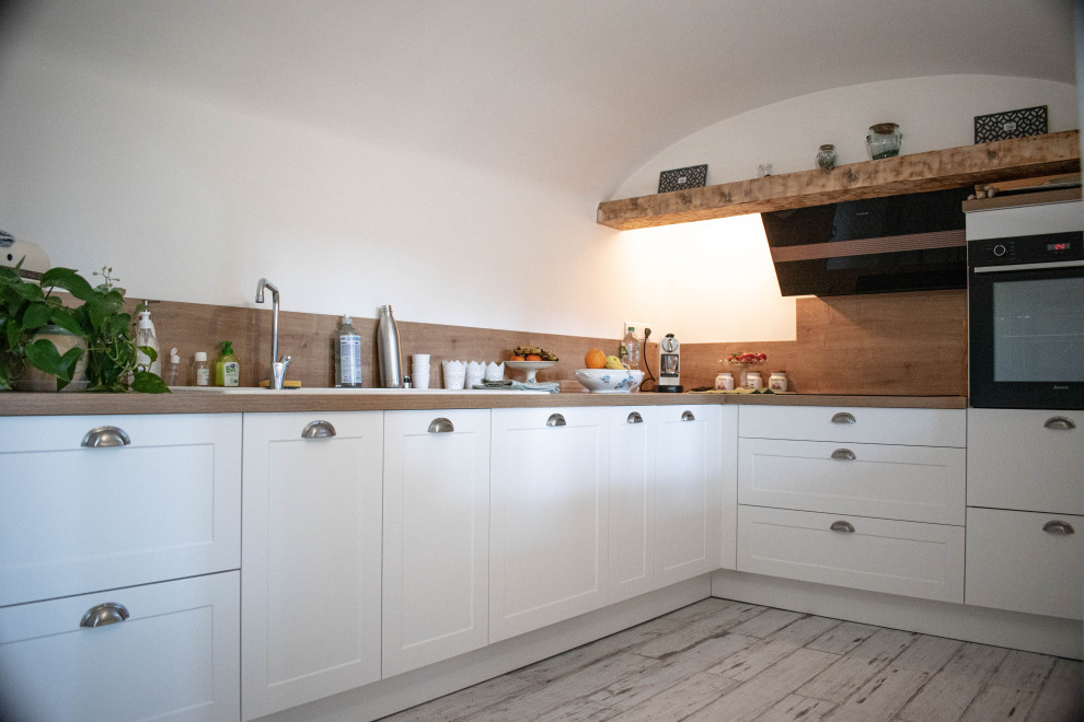 Mid-sized transitional l-shaped separate kitchen in Marseille with a single-bowl sink, shaker cabinets, white cabinets, laminate benchtops, brown splashback, timber splashback, black appliances, plywood floors, no island, white floor, brown benchtop and vaulted.