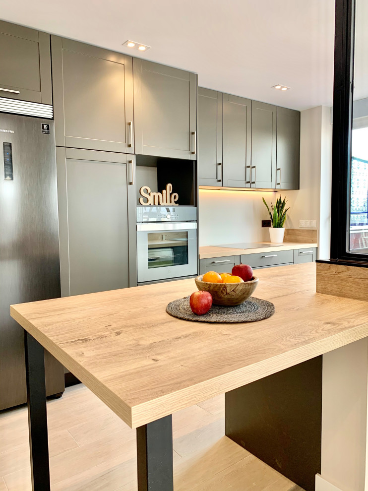 Photo of a mid-sized contemporary single-wall open plan kitchen in Madrid with a single-bowl sink, raised-panel cabinets, grey cabinets, laminate benchtops, beige splashback, window splashback, stainless steel appliances, porcelain floors, beige floor and beige benchtop.