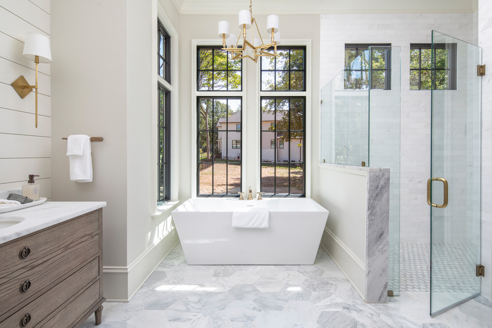 Large transitional master bathroom in Charlotte with furniture-like cabinets, medium wood cabinets, a freestanding tub, a corner shower, white tile, marble, beige walls, marble floors, an undermount sink, marble benchtops, a hinged shower door and white benchtops.