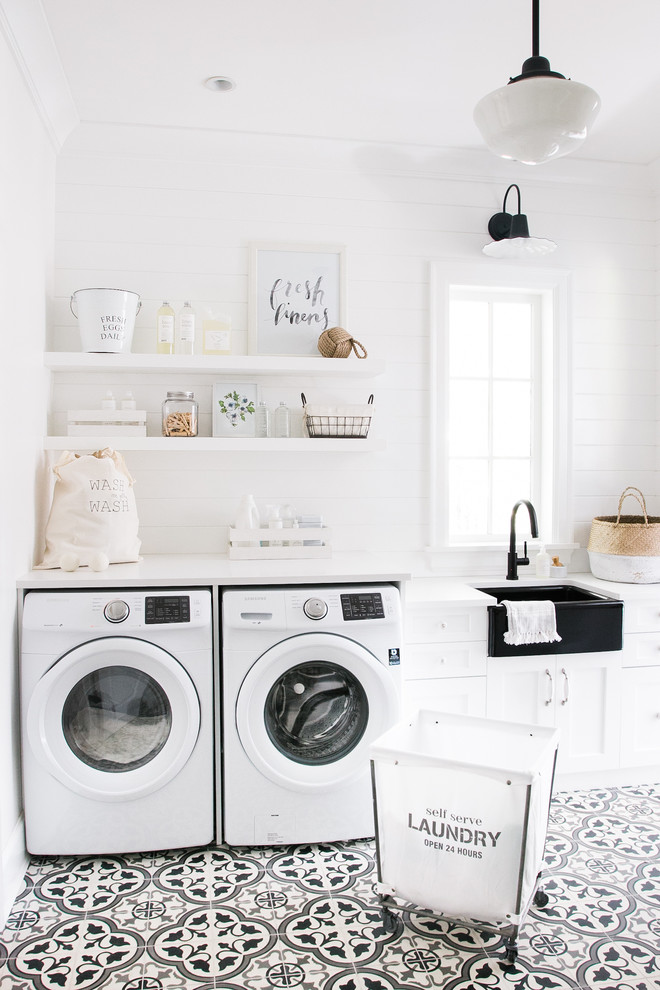 This is an example of a large country single-wall dedicated laundry room in Vancouver with a farmhouse sink, recessed-panel cabinets, white cabinets, marble benchtops, white walls, ceramic floors, a side-by-side washer and dryer, black floor and white benchtop.