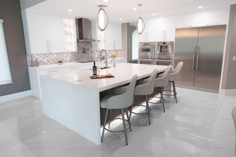 Photo of a large modern kitchen in Miami with a single-bowl sink, flat-panel cabinets, white cabinets, quartz benchtops, grey splashback, marble splashback, stainless steel appliances, porcelain floors, with island, white floor and white benchtop.