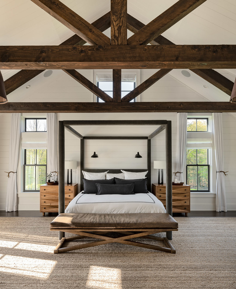 This is an example of a large country master bedroom in New York with white walls, dark hardwood floors and brown floor.