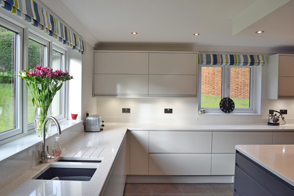 Design ideas for a modern kitchen/diner with flat-panel cabinets, grey cabinets, quartz worktops, white splashback, integrated appliances and an island.