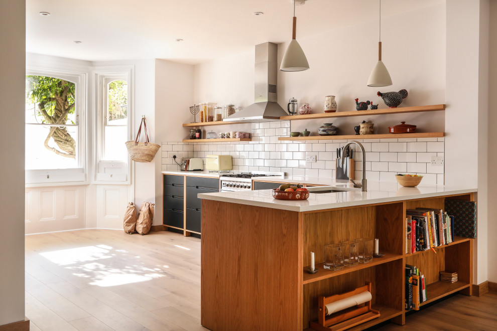 Inspiration for a large scandinavian l-shaped kitchen in London with an undermount sink, flat-panel cabinets, black cabinets, white splashback, subway tile splashback, stainless steel appliances, light hardwood floors, a peninsula, beige floor and white benchtop.