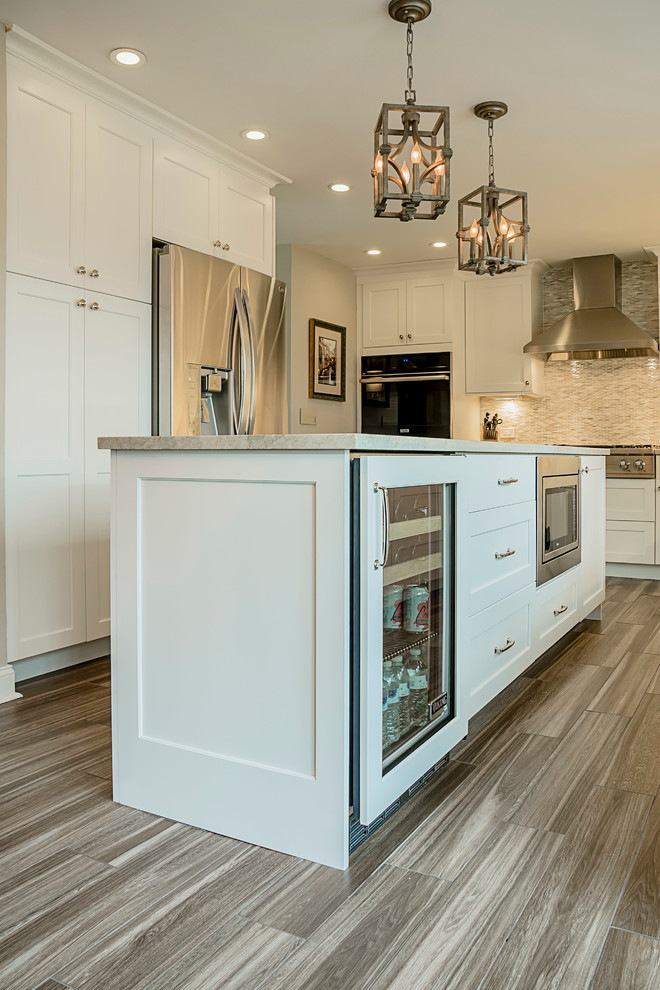 Eat-in kitchen - large transitional galley porcelain tile eat-in kitchen idea in Chicago with a farmhouse sink, shaker cabinets, white cabinets, quartzite countertops, multicolored backsplash, glass sheet backsplash, stainless steel appliances and an island