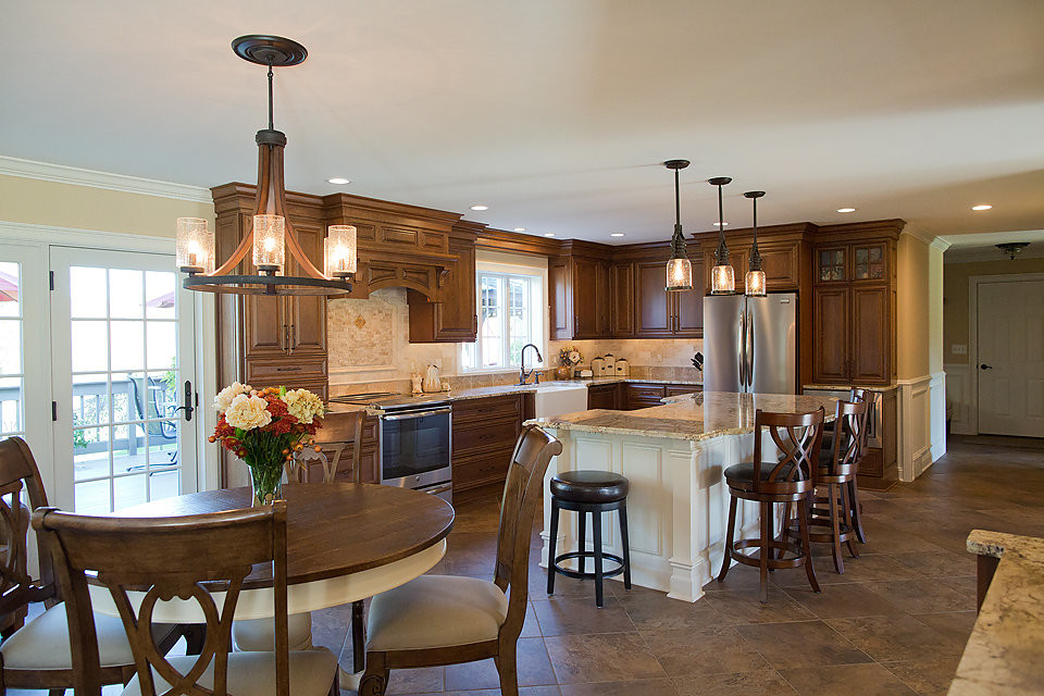 This is an example of a large traditional l-shaped eat-in kitchen in Boston with a farmhouse sink, dark wood cabinets, granite benchtops, beige splashback, porcelain splashback, stainless steel appliances, porcelain floors and with island.